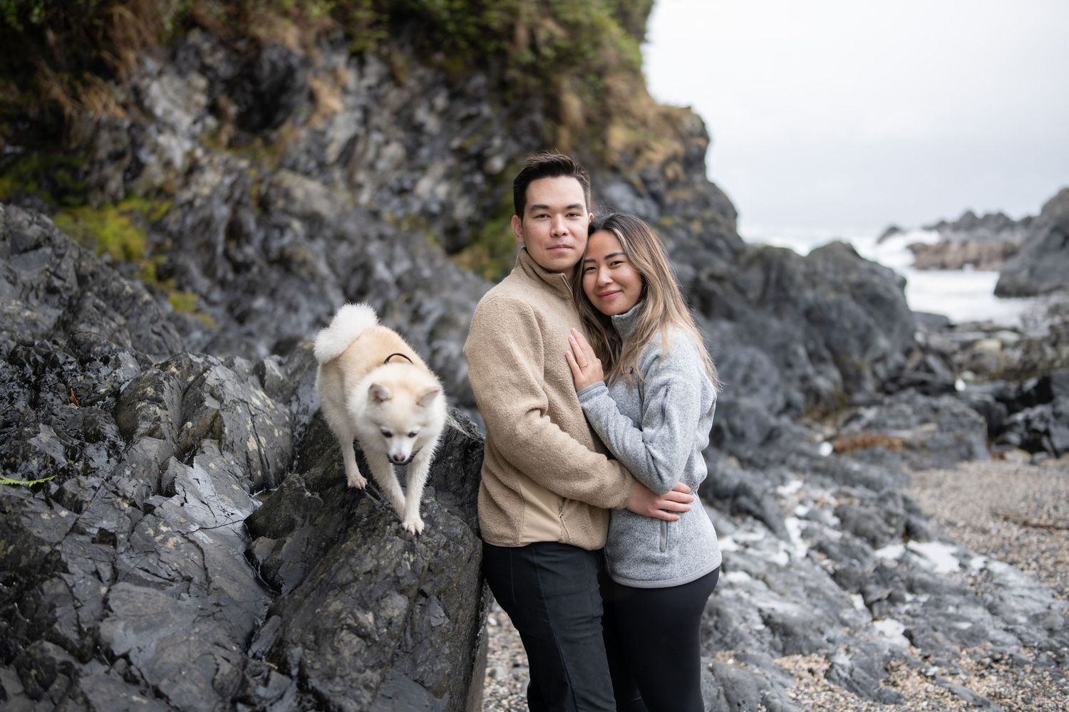 Couple standing among dramatic black rocks on a moody beach coastline.