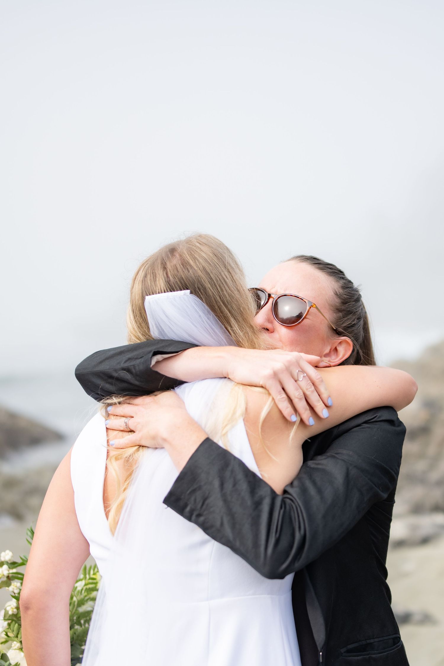 Close-up of emotional wedding embrace against bright coastal background.