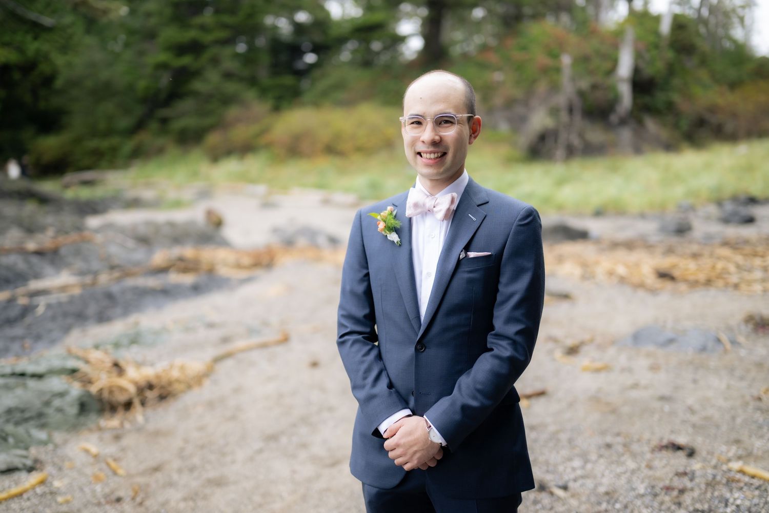 Person in formal attire standing on rocky coastal terrain.