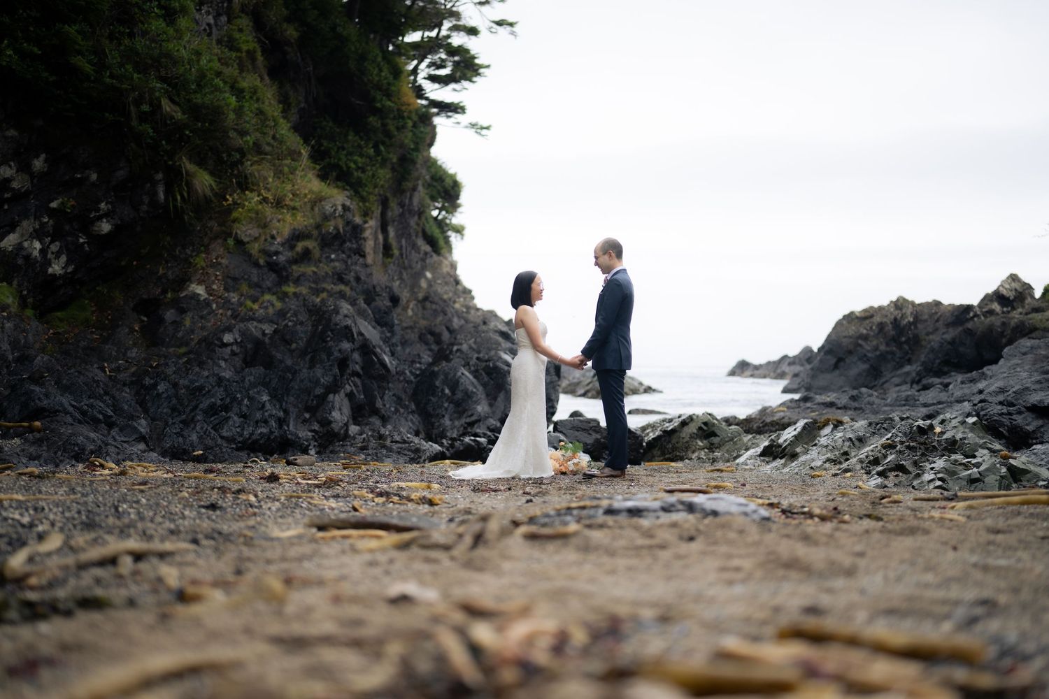 Wedding couple celebrates their ceremony on a dramatic rocky beach with coastal views.