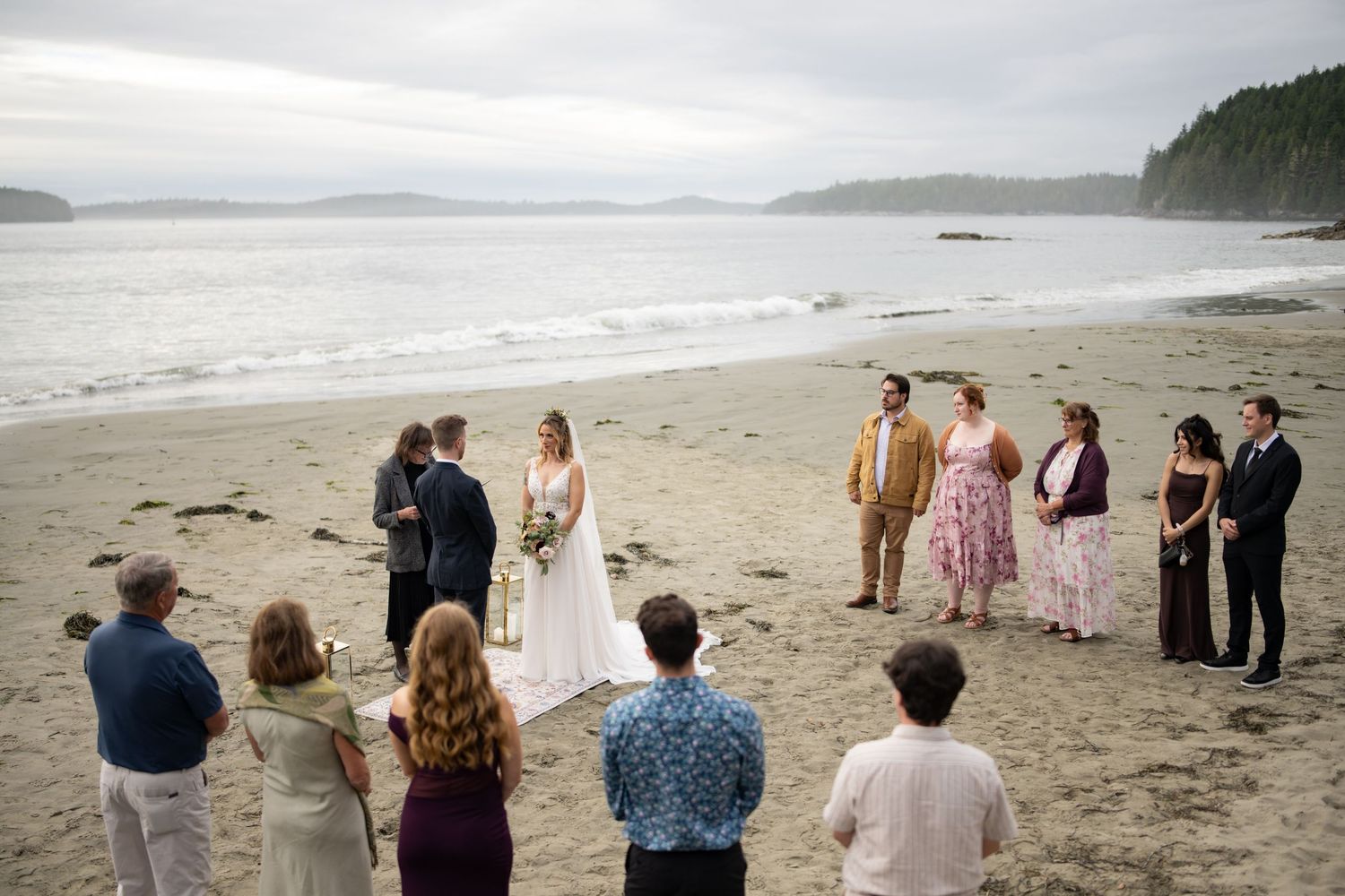 Small group gathers for beach ceremony against cloudy coastal backdrop.