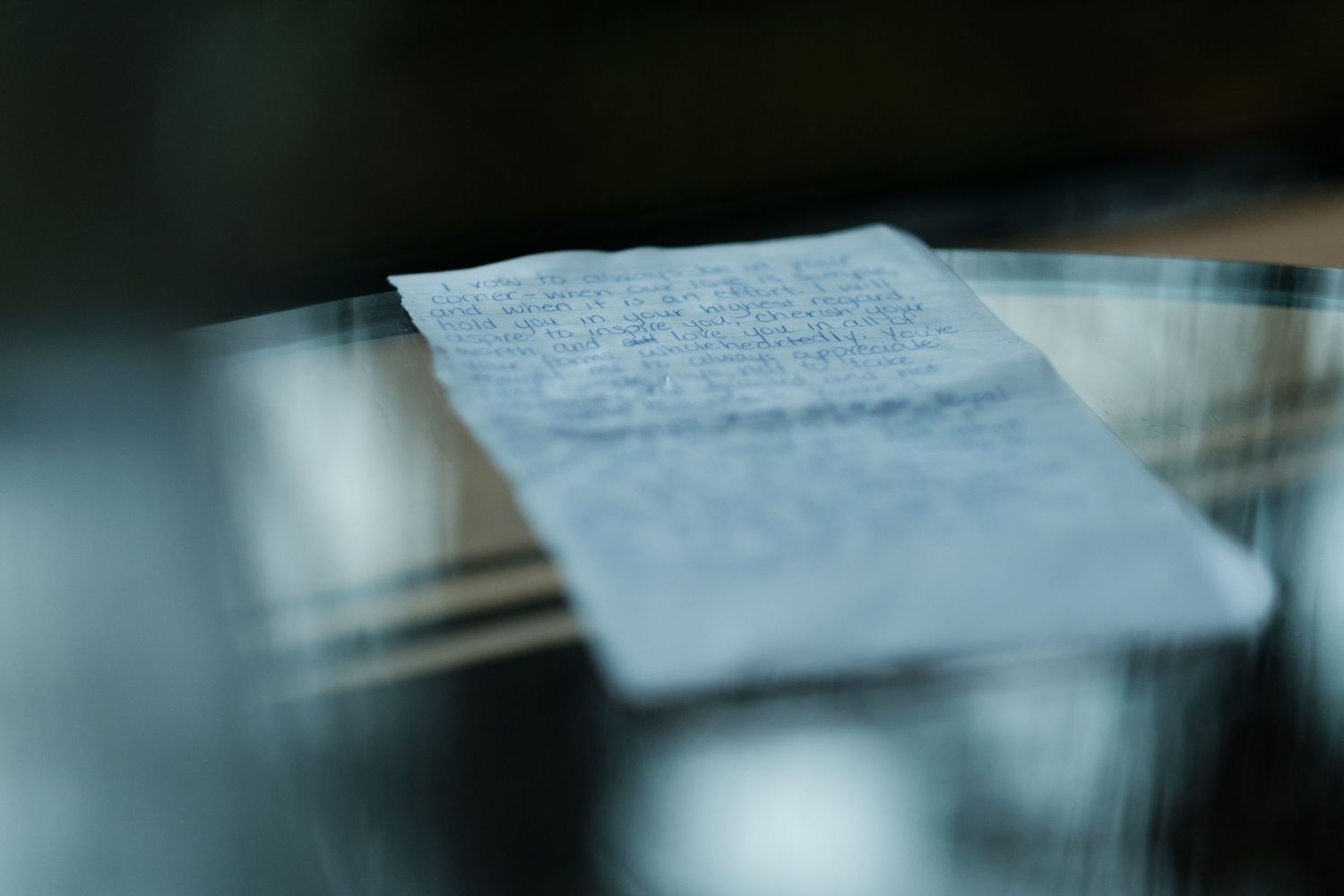 A handwritten letter or note lies on a reflective surface in soft focus.