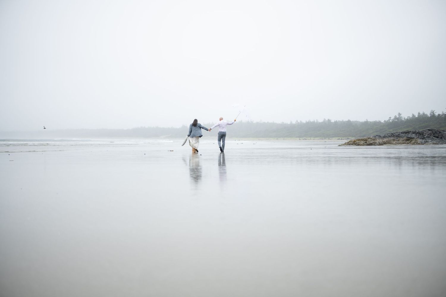 Distant figures walking with umbrellas along a misty Pacific Northwest beach.