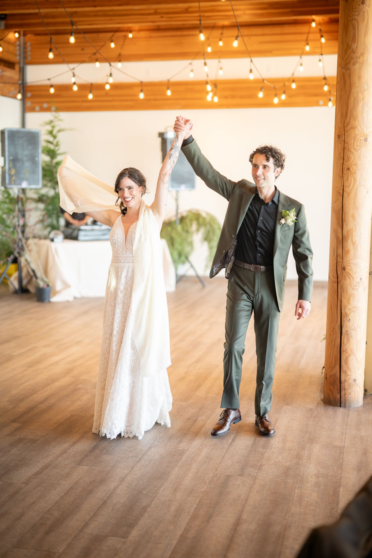 Celebratory moment on wooden dance floor under string lights at reception venue.