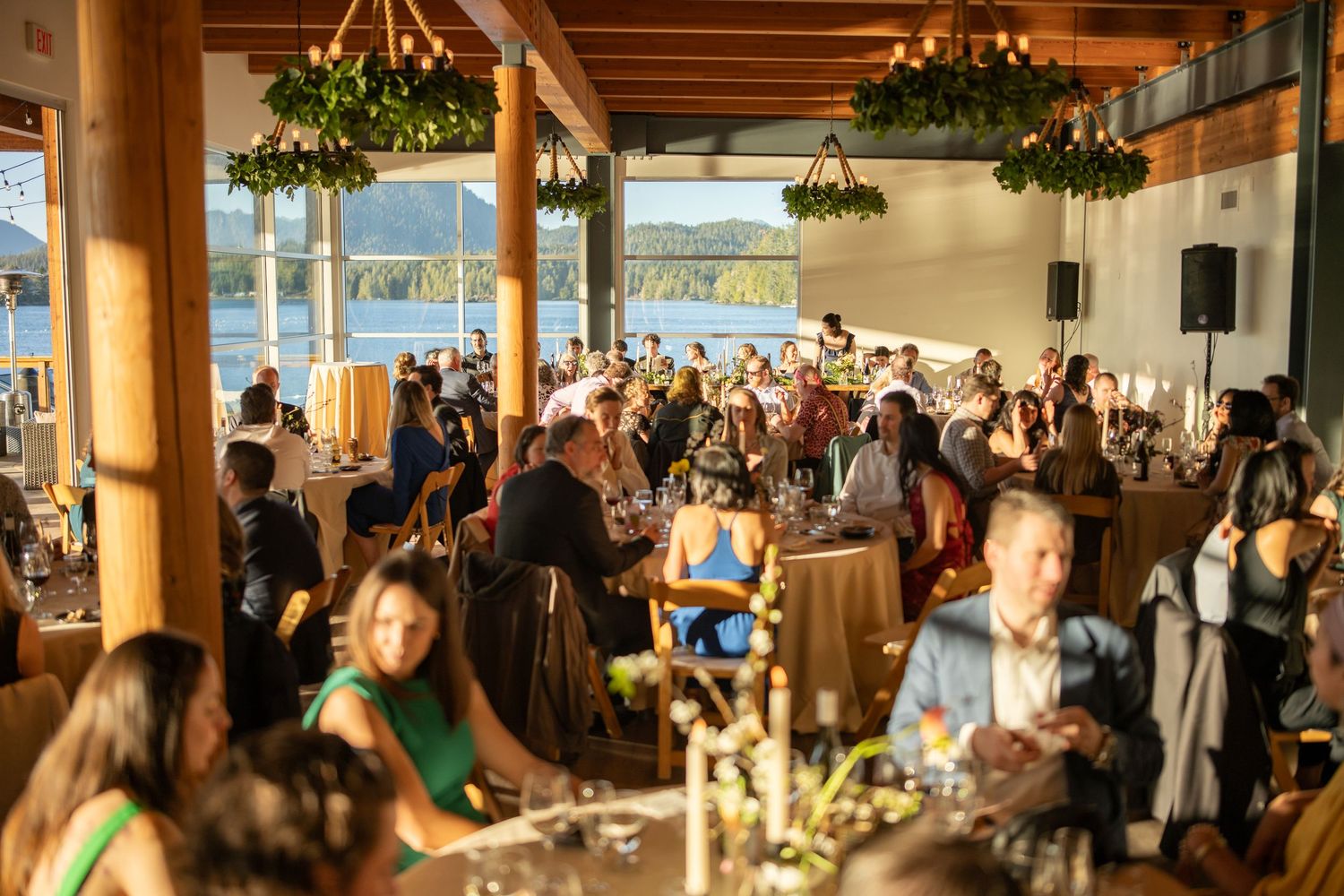 Large wedding reception hall with exposed wooden beams and decorative greenery.