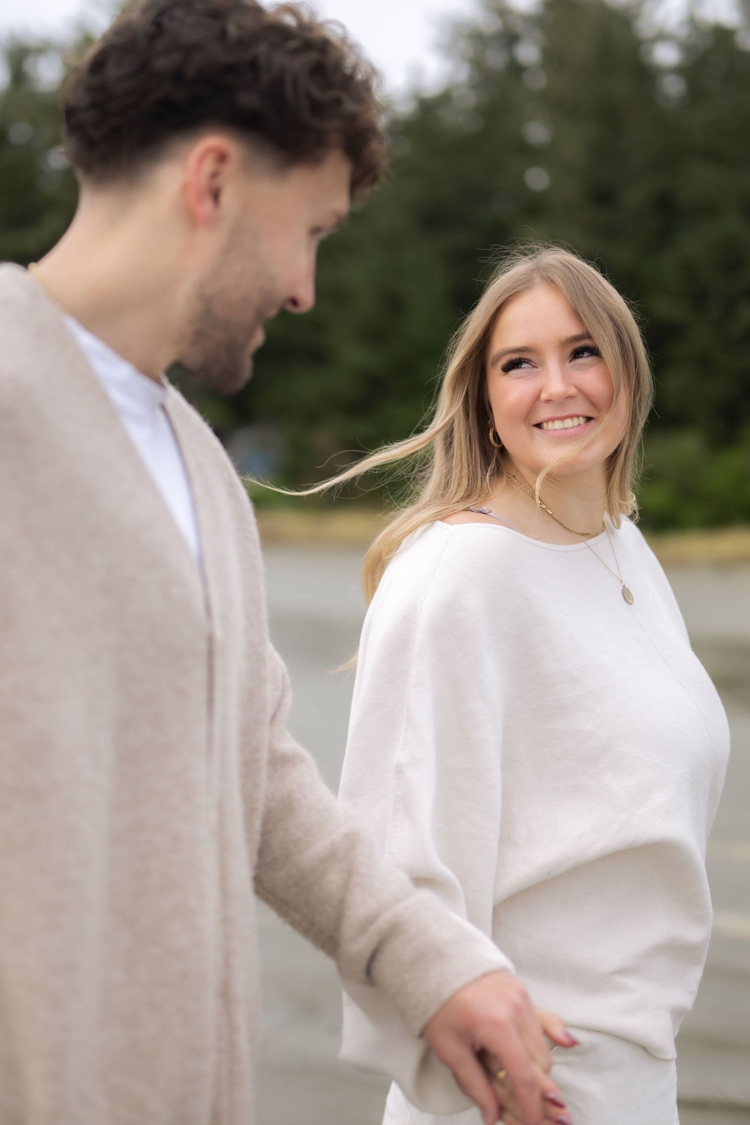 A tender moment captured between two people in matching cream colored sweaters on a coastal beach.