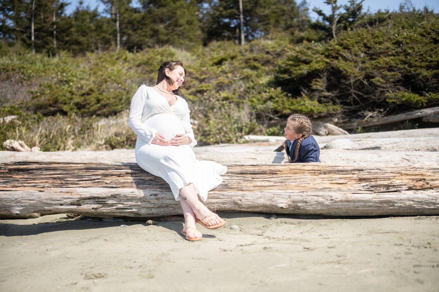 People relax on weathered driftwood logs scattered along a pristine beach shoreline.