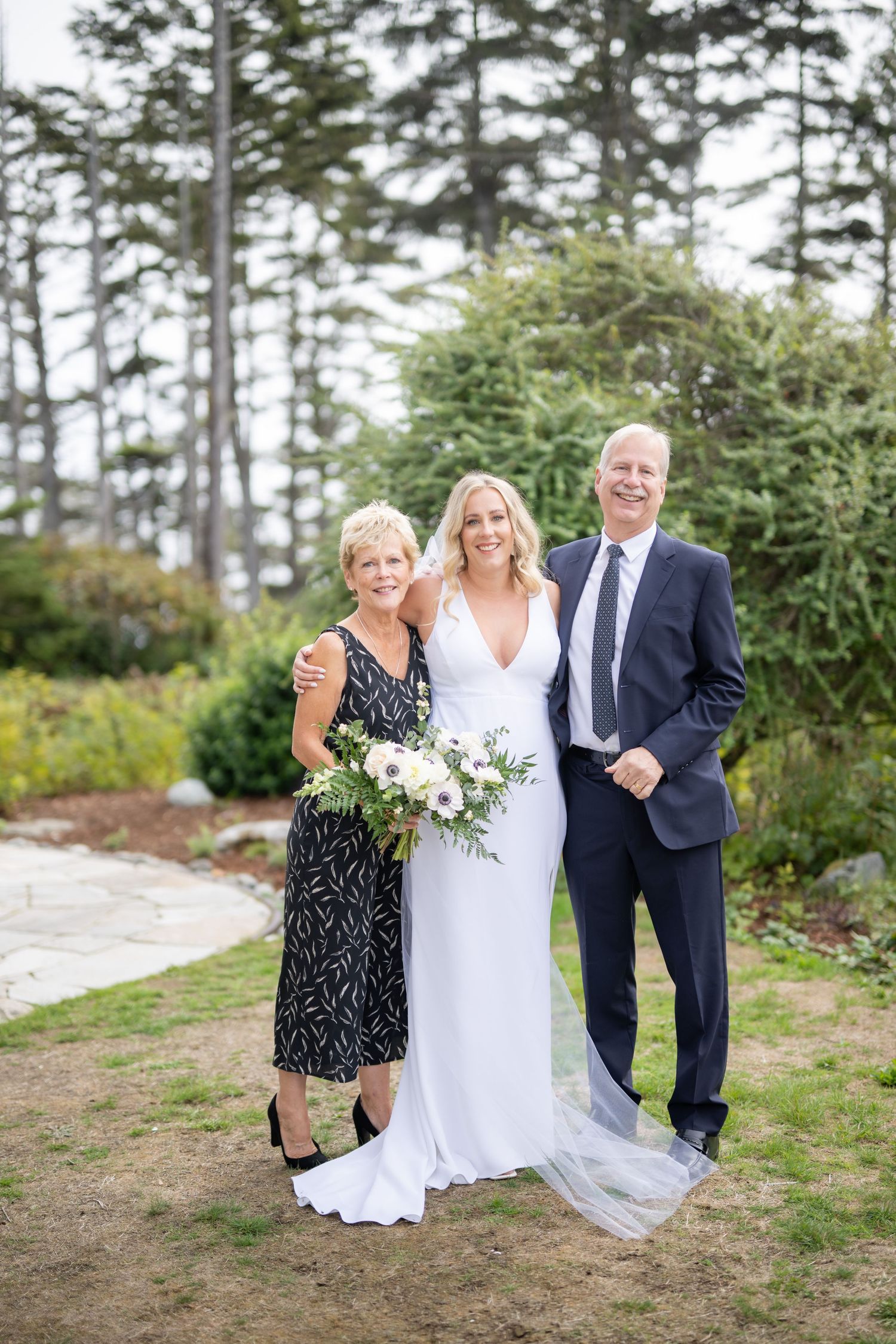 Wedding party poses together on natural terrain with pine trees in background.
