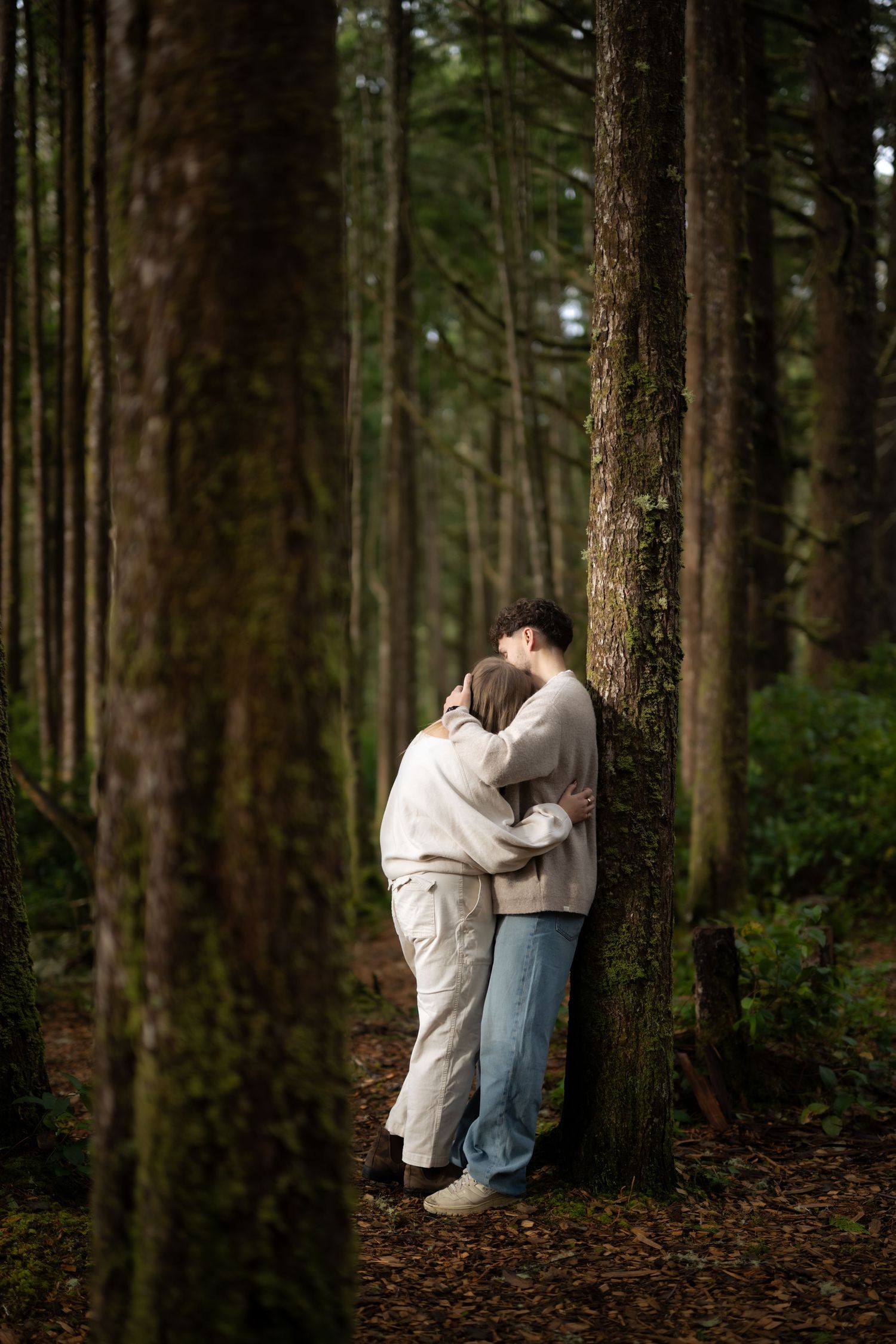 Intimate forest portrait of couple in casual attire among towering pine trees.