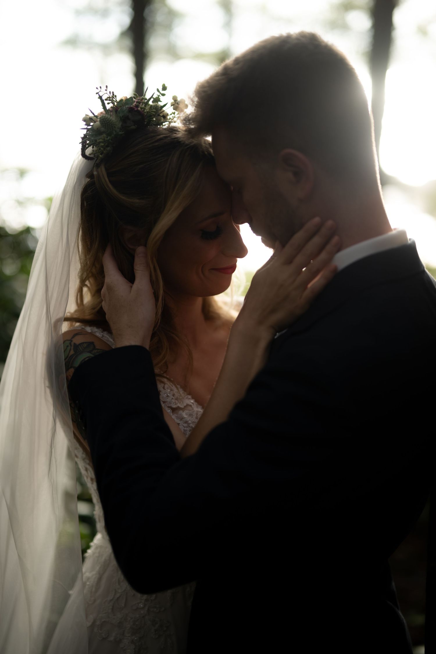 Romantic silhouetted wedding portrait with soft backlight through trees.