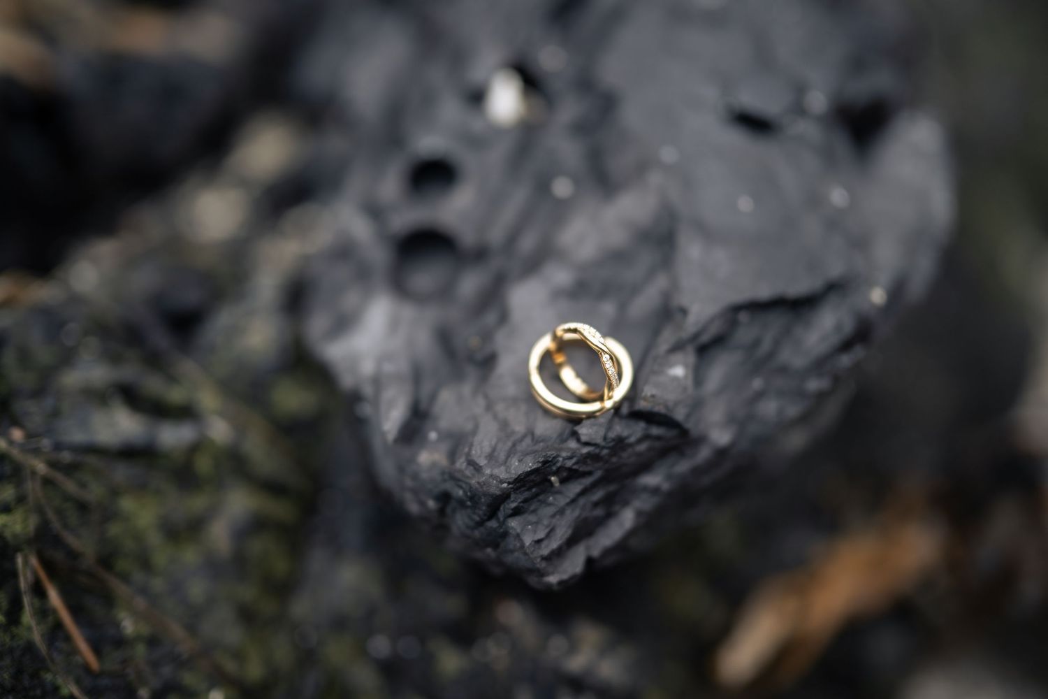 Wedding rings displayed on dark volcanic rock with natural textures.