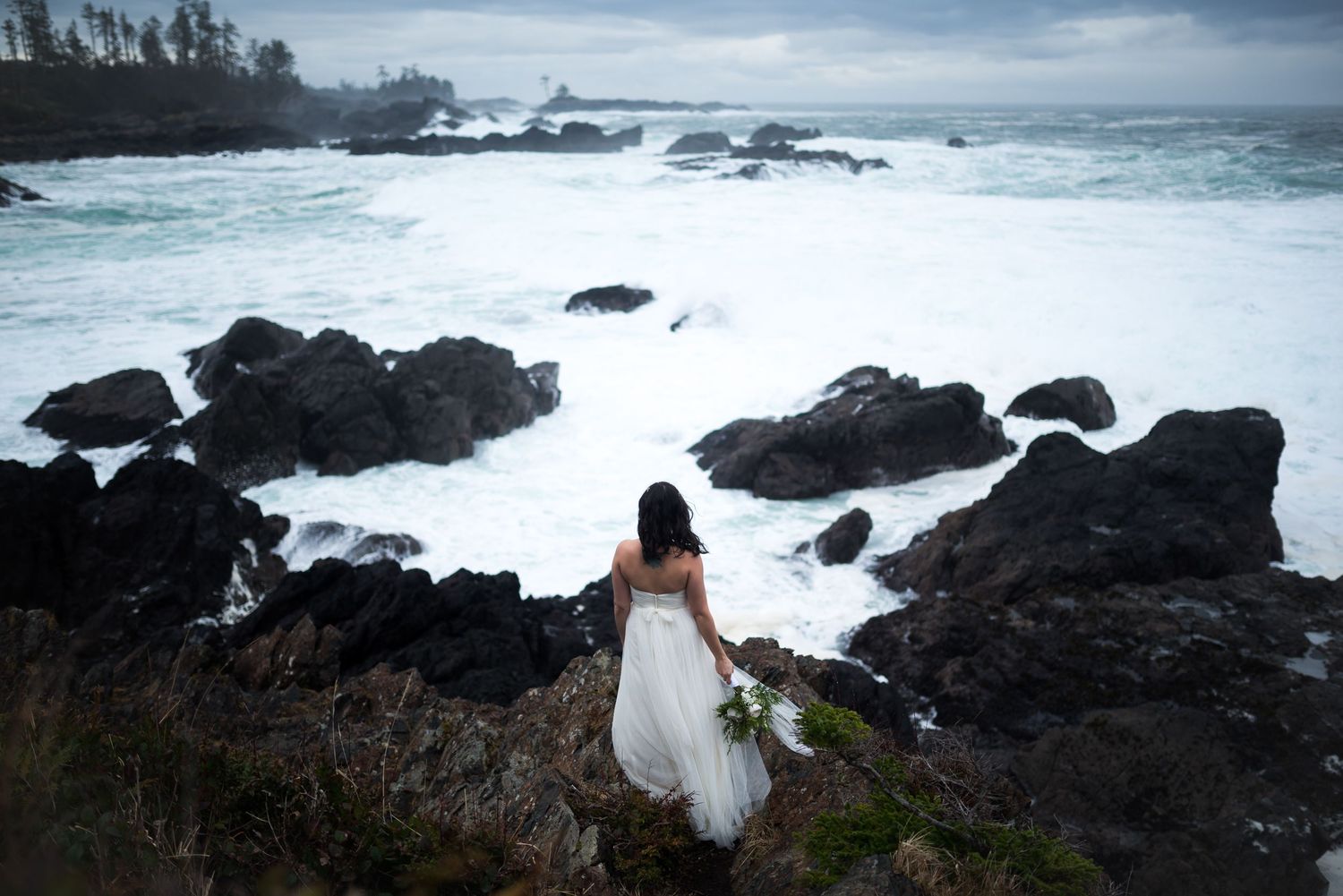 Dramatic coastal wedding portrait with rocky shoreline and crashing waves.