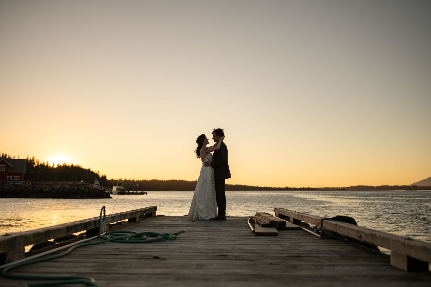 Silhouettes on a dock at sunset with mountains and water creating a romantic backdrop.