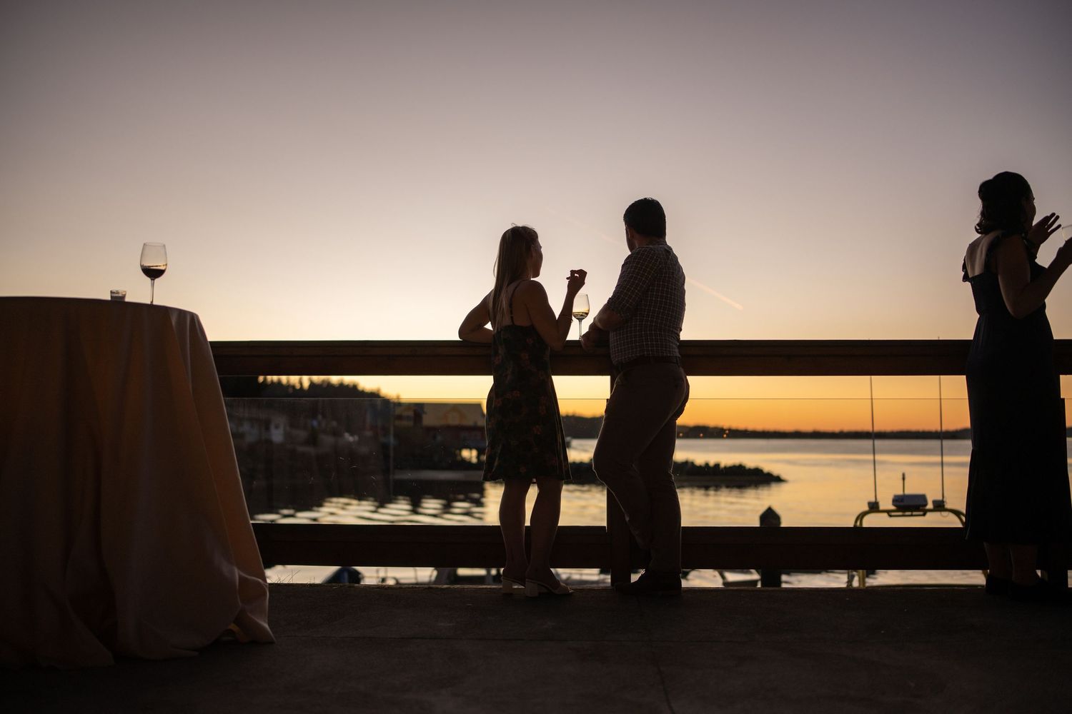 Silhouettes of guests mingling during sunset against a waterfront backdrop.
