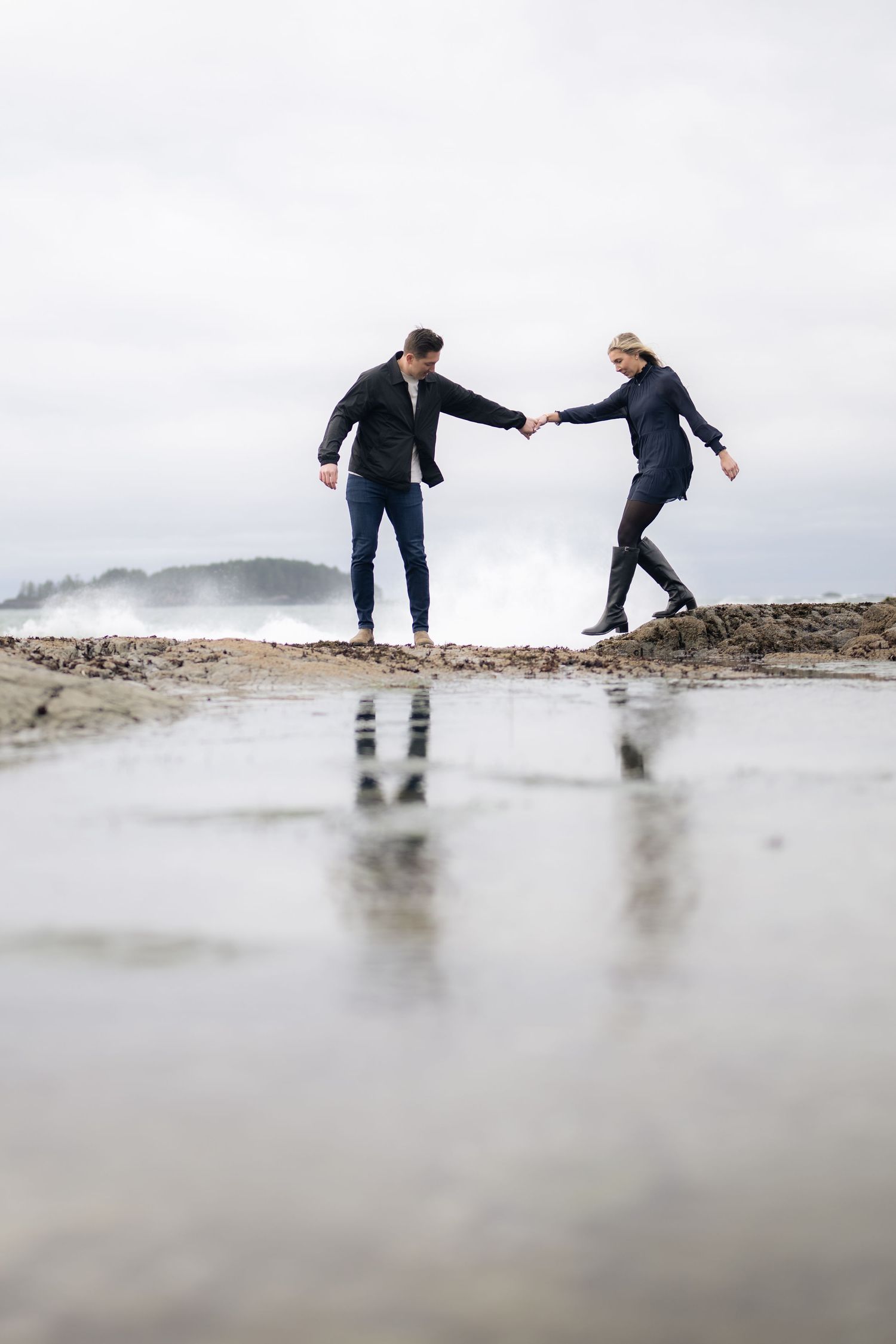 Two people hold hands while playing in shallow water on a beach.