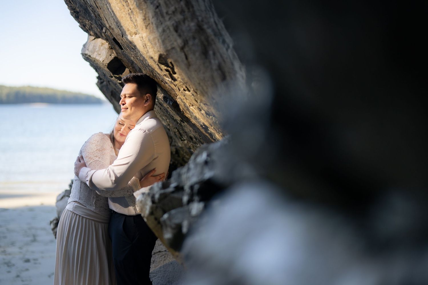 Two people share a moment under a dramatic rock overhang by the ocean.