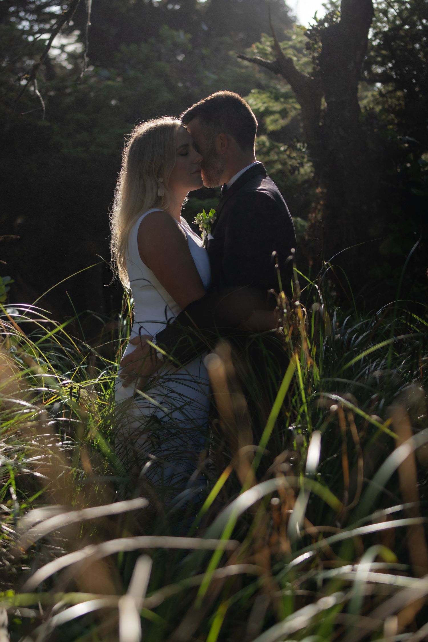 Romantic moment between newlyweds among tall grass at golden hour.