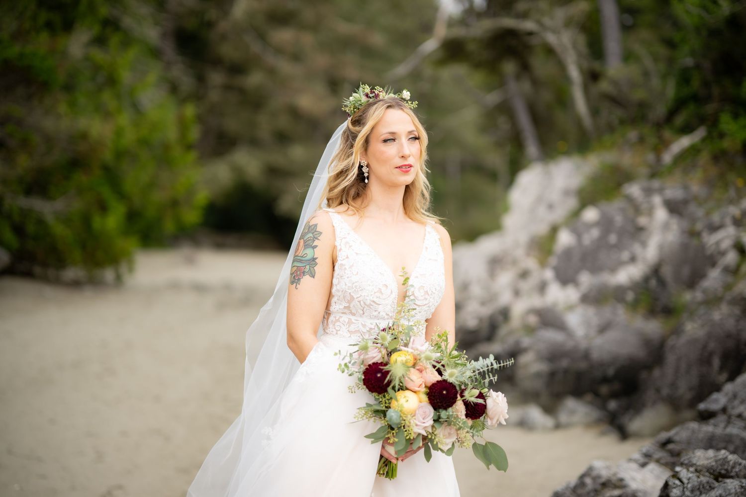 A bridal bouquet with burgundy and cream flowers stands out against a white lace dress.