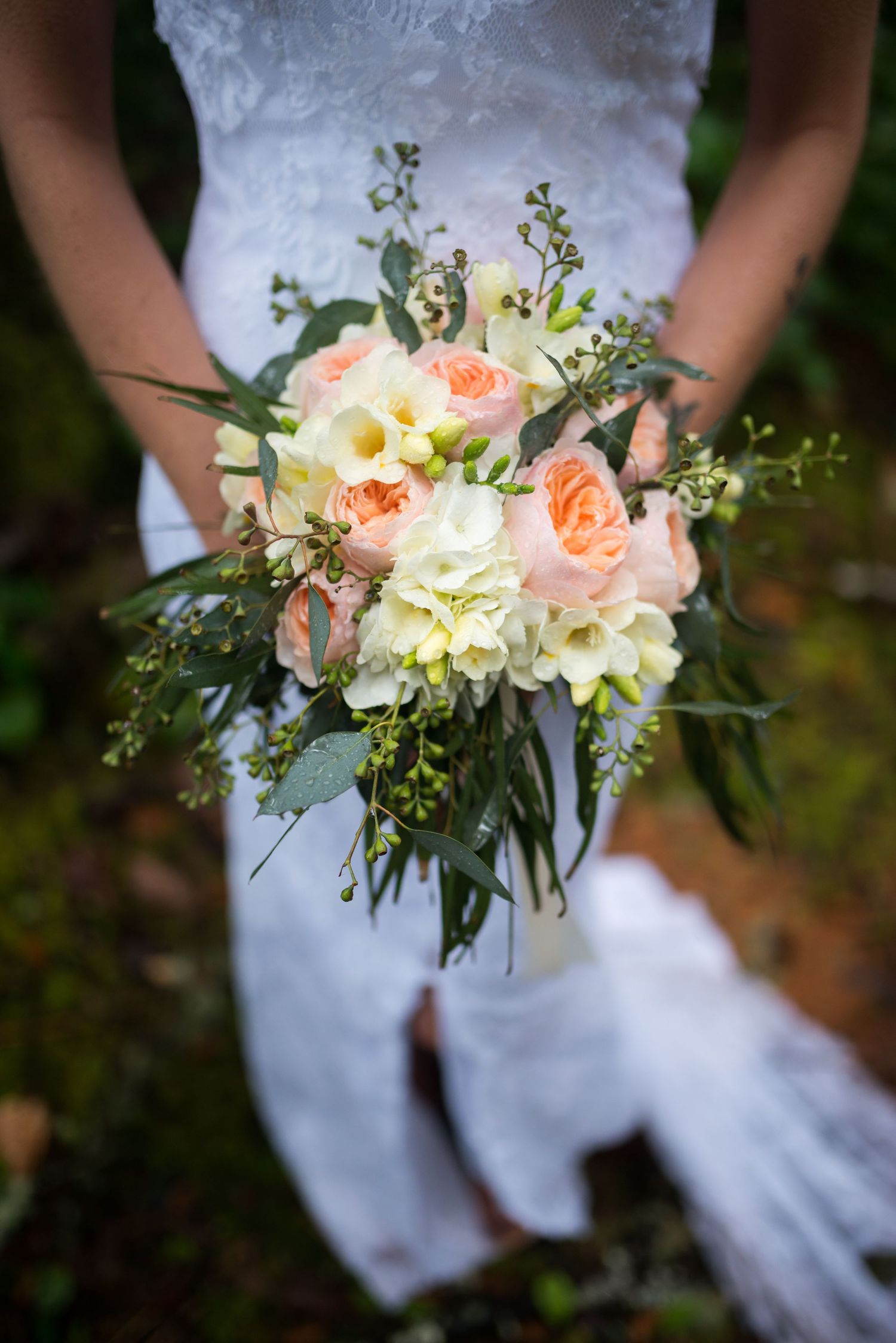 Beautiful wedding bouquet with peach and white flowers against a white dress.