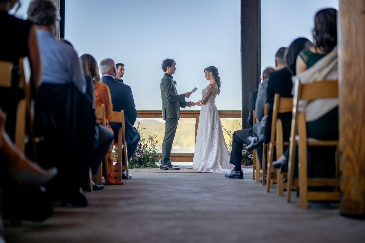 Indoor wedding ceremony with guests seated in wooden chairs facing scenic mountain views.