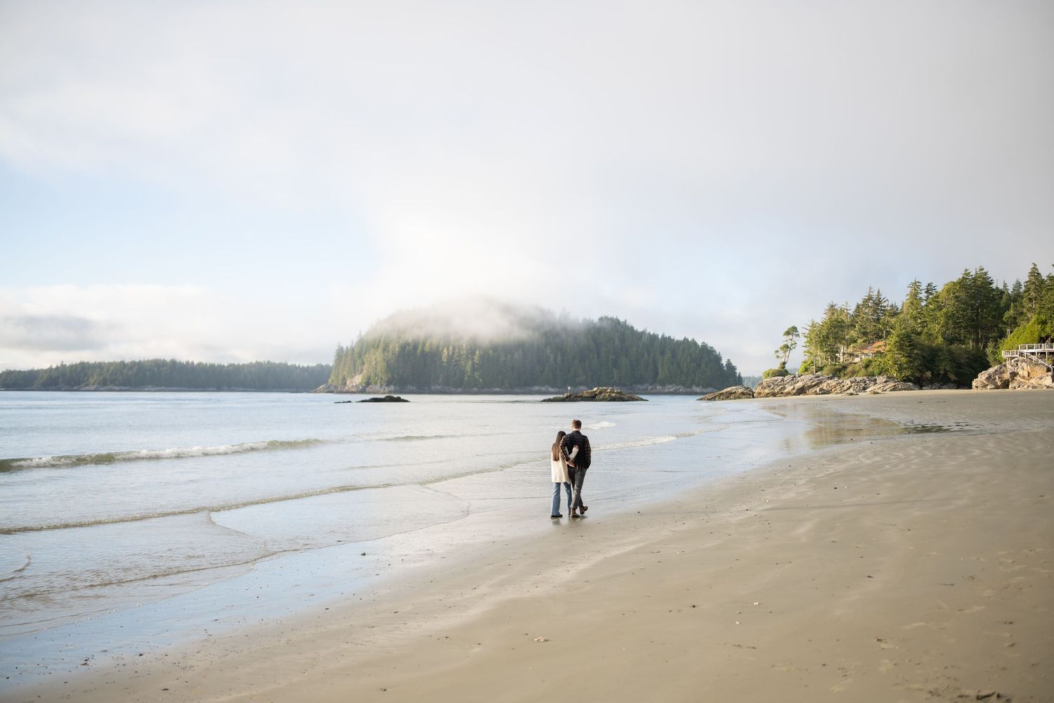 Two people walking along misty Pacific Northwest beach at sunrise.