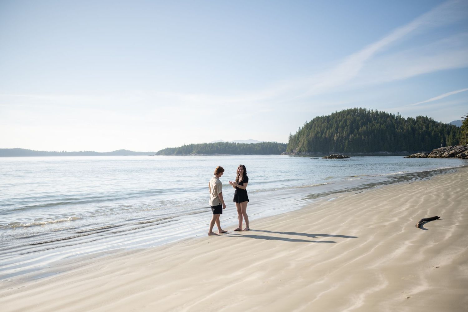 People walking along a pristine sandy beach with forested islands in the distance.