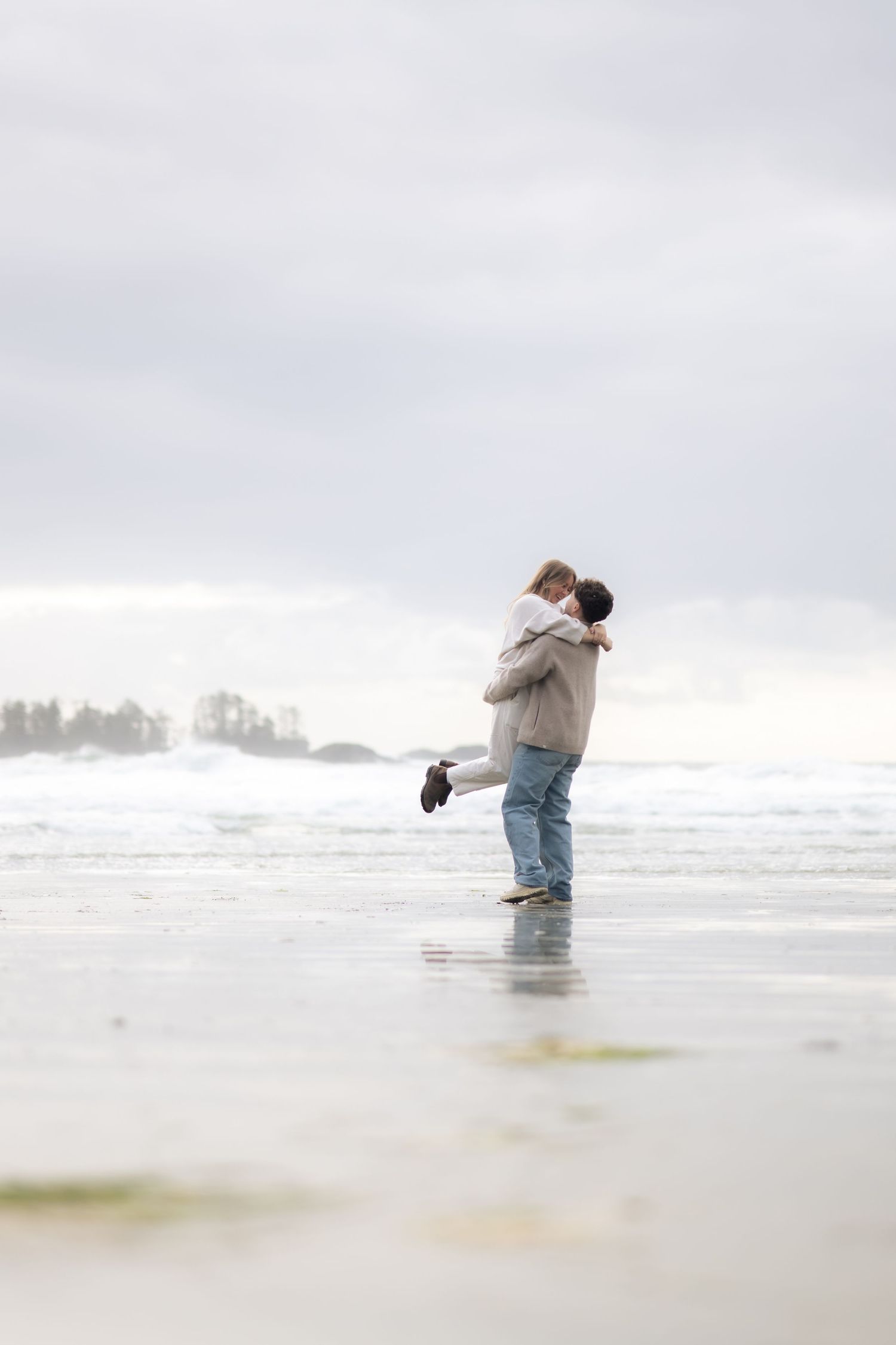 A person takes photos of crashing waves on a misty beach shoreline.
