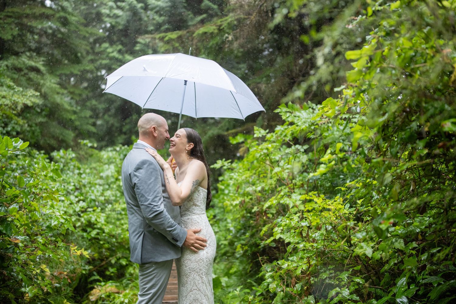 A romantic moment shared under a white umbrella in a misty green forest setting.