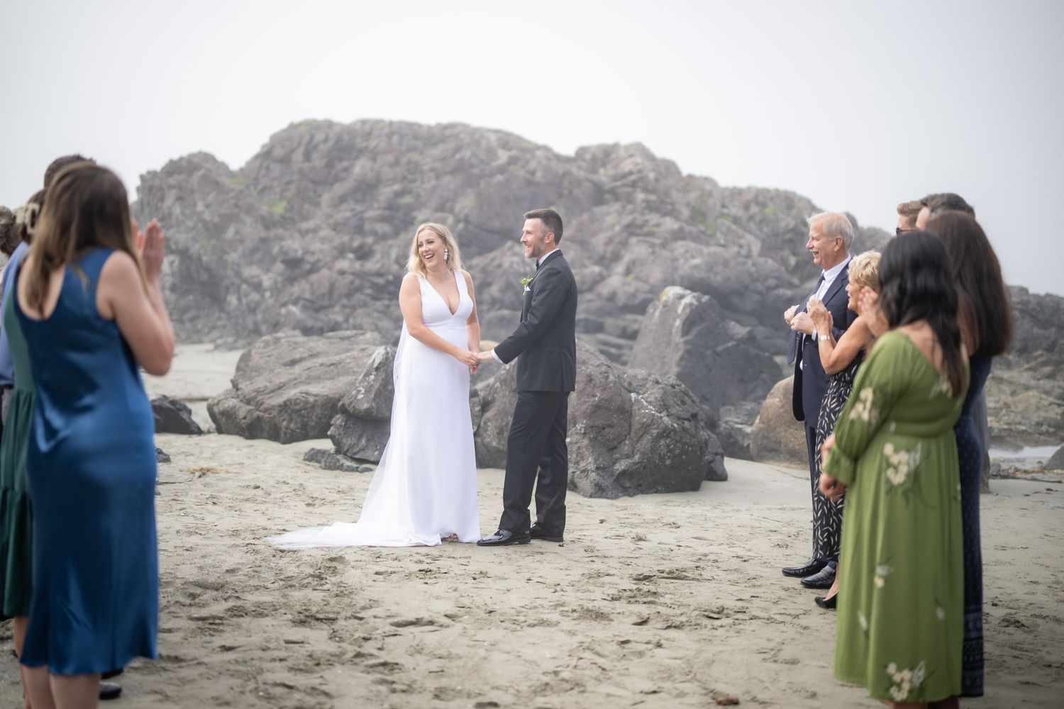Guests in formal attire attend a seaside wedding ceremony near rocky cliffs.
