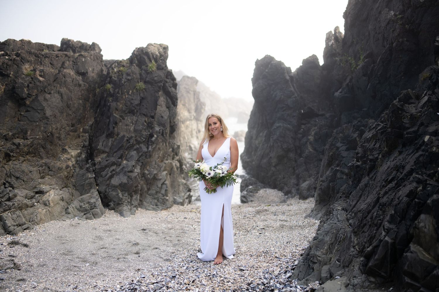 Wedding couple walks through scenic rocky beach cove surrounded by cliffs.
