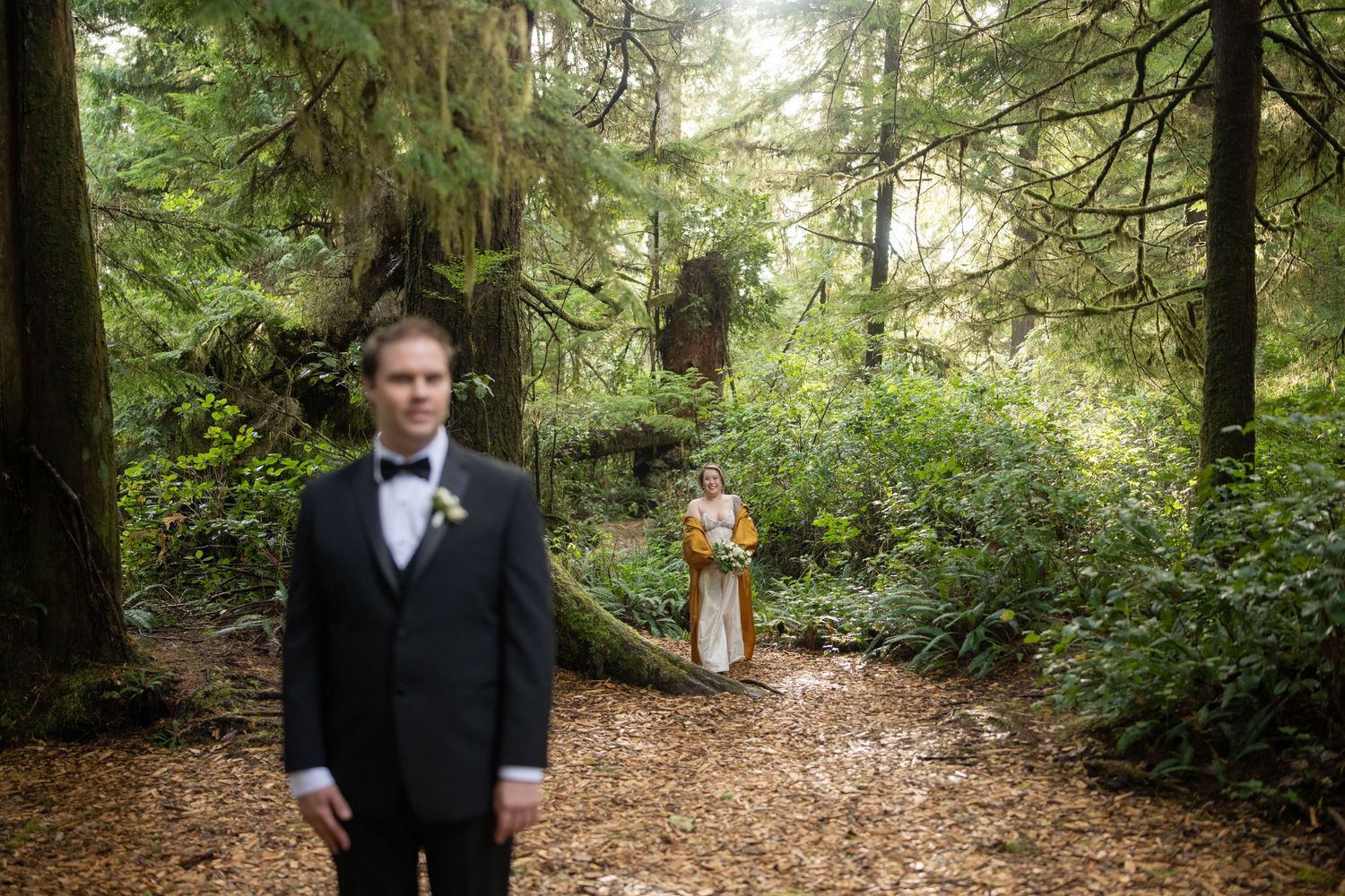 A formal wedding moment captured on a winding forest path surrounded by towering evergreens.