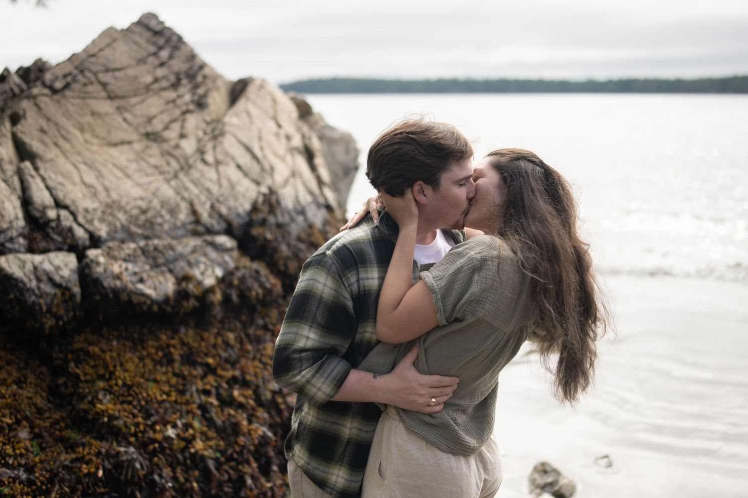 A romantic embrace captured on a scenic beach with ocean waves and rocky shore.