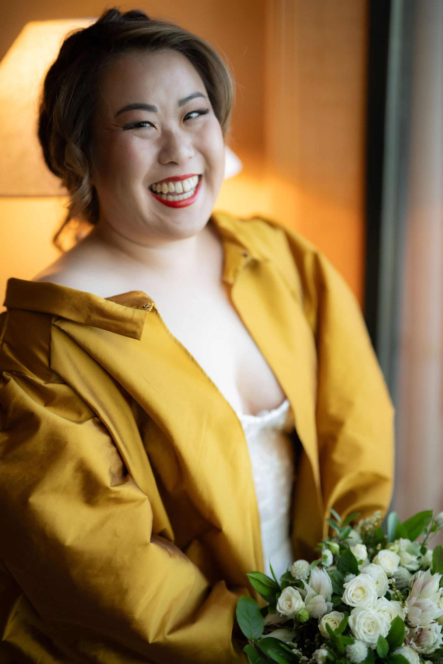 Person in bright yellow jacket holding white floral bouquet with joyful expression.