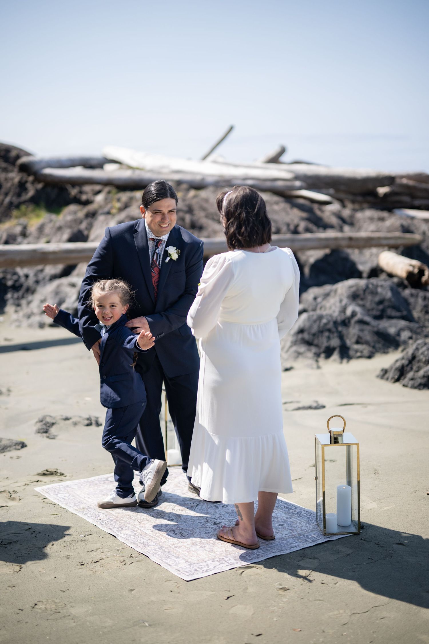An intimate beach wedding ceremony with decorative lanterns and a blanket laid out on the sand.