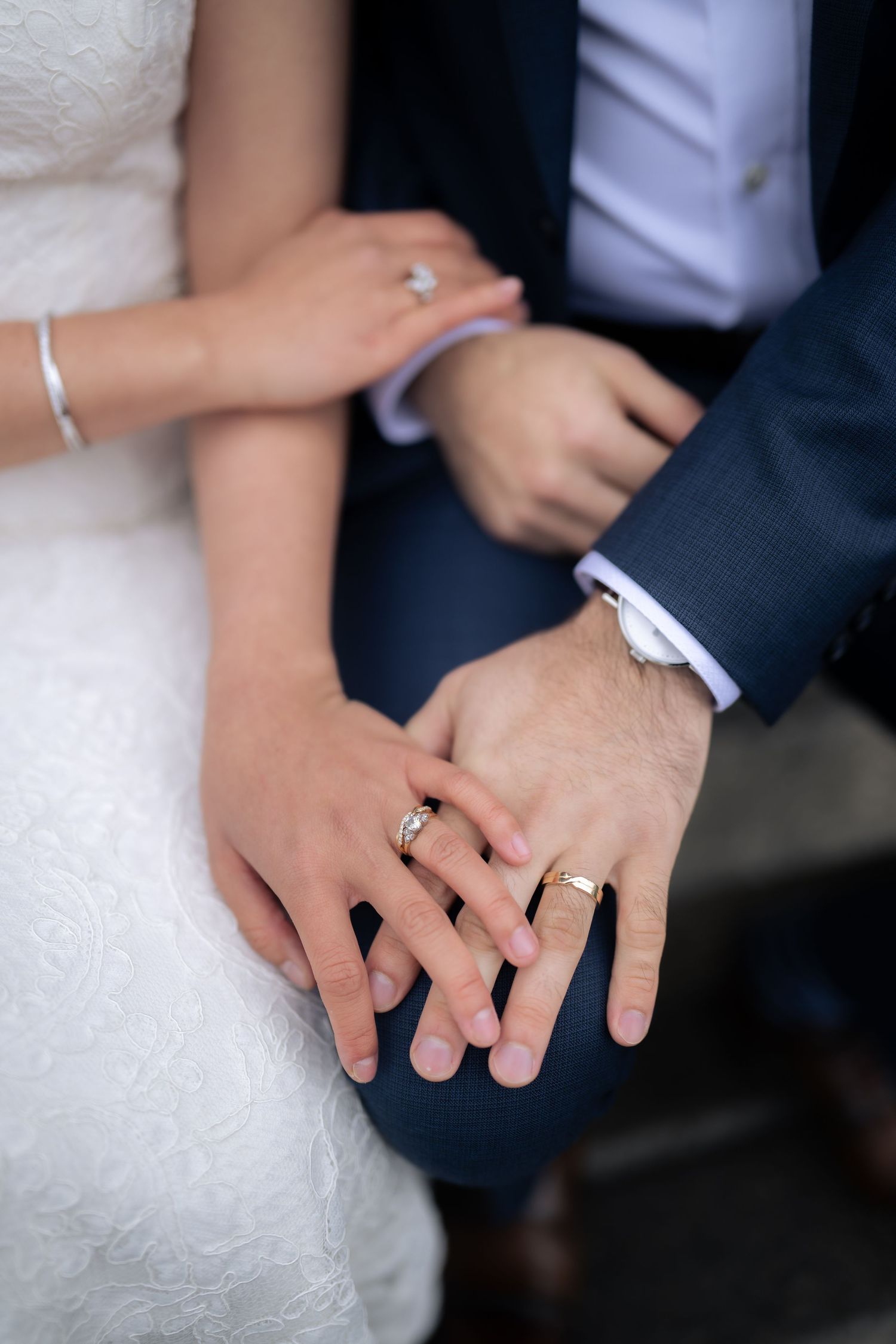 Close-up of hands wearing wedding rings resting together on formal attire.