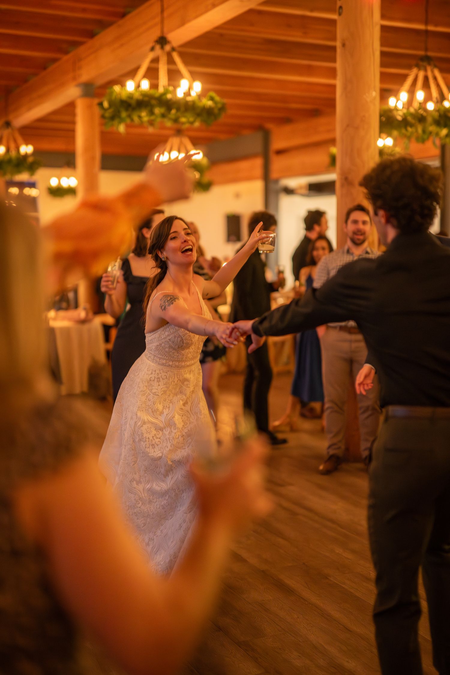 Joyful dancing and celebration at a wedding reception in a rustic venue with wooden beams.