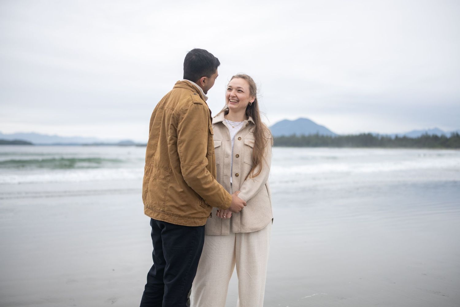 Couple embracing on a windswept beach with dramatic mountain scenery.