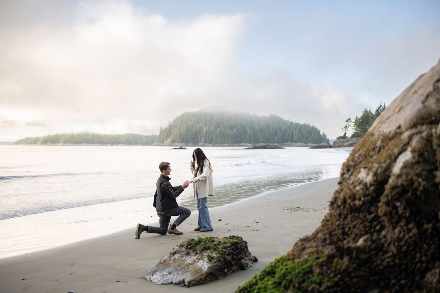 Dramatic coastal landscape with rocky outcrops and figures on a misty beach.