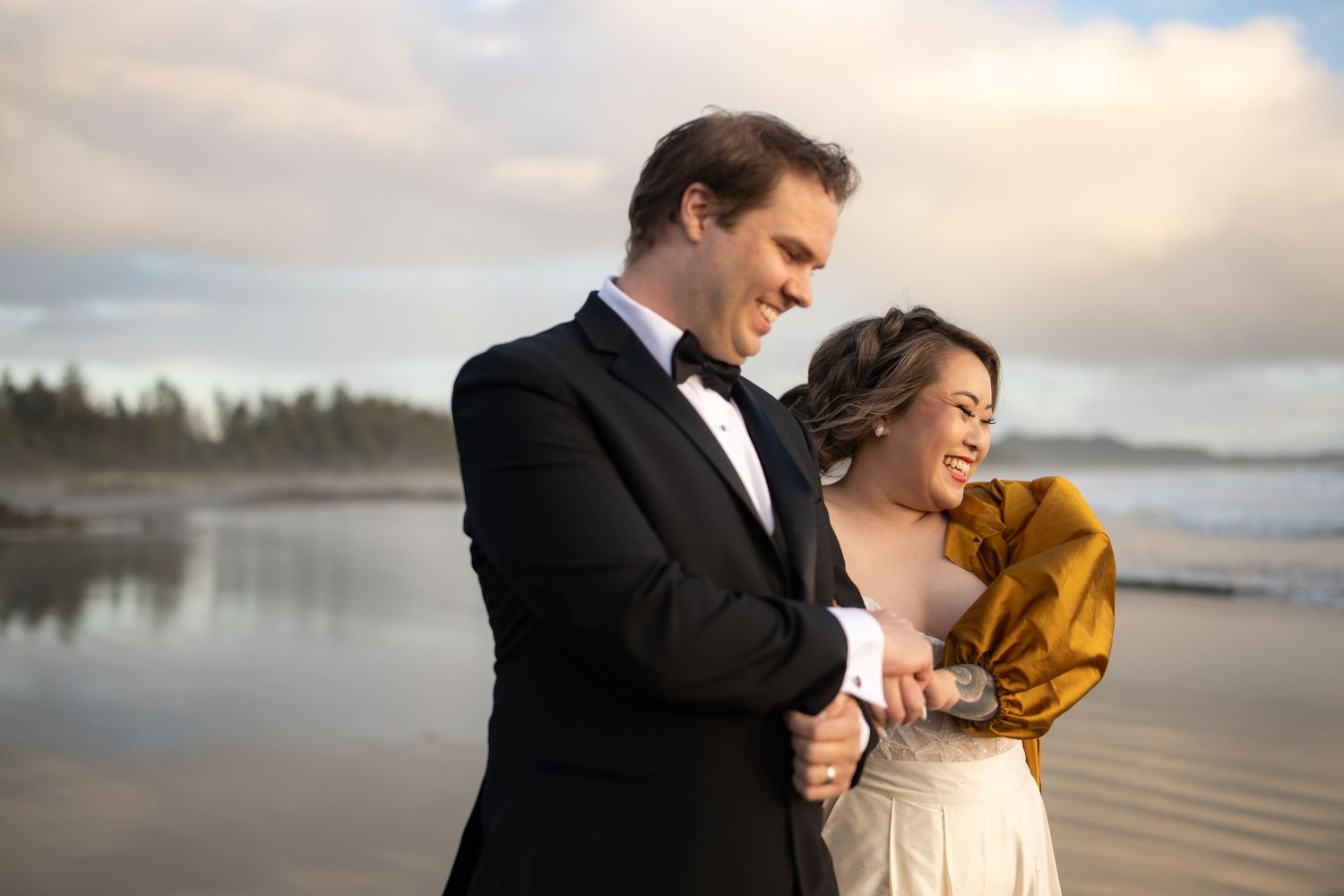 A joyful moment shared between two people in formal wear on a cloudy beach.