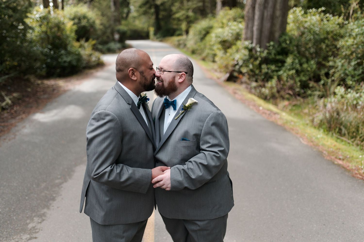 Couple shares tender moment on tree-lined path wearing matching grey suits.