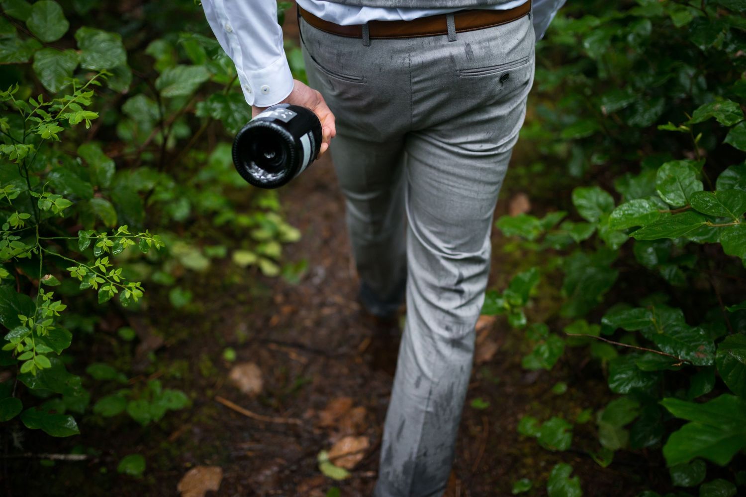 A person in formal wear carries a camera through forest vegetation.