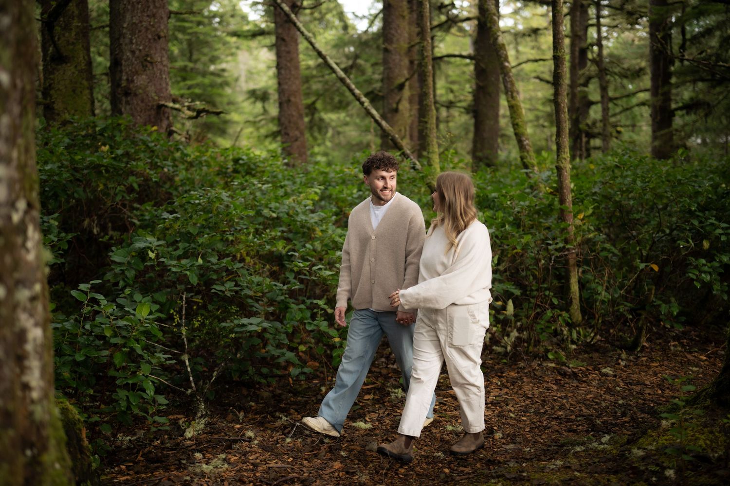 Couple in light colored clothing walking through a wooded forest setting.