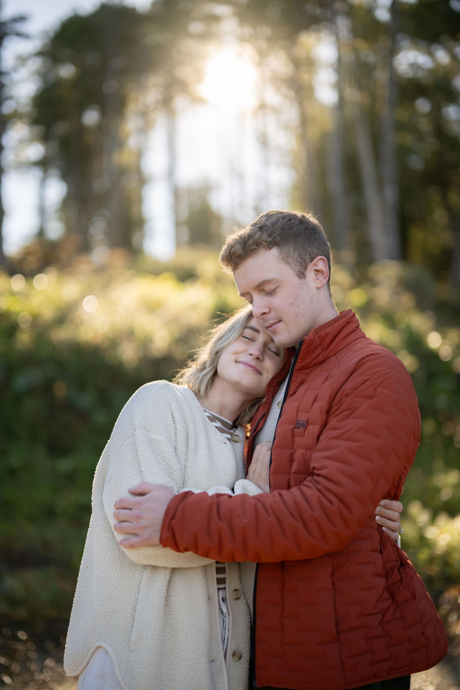 Two people share tender moments in a sunlit forest setting.