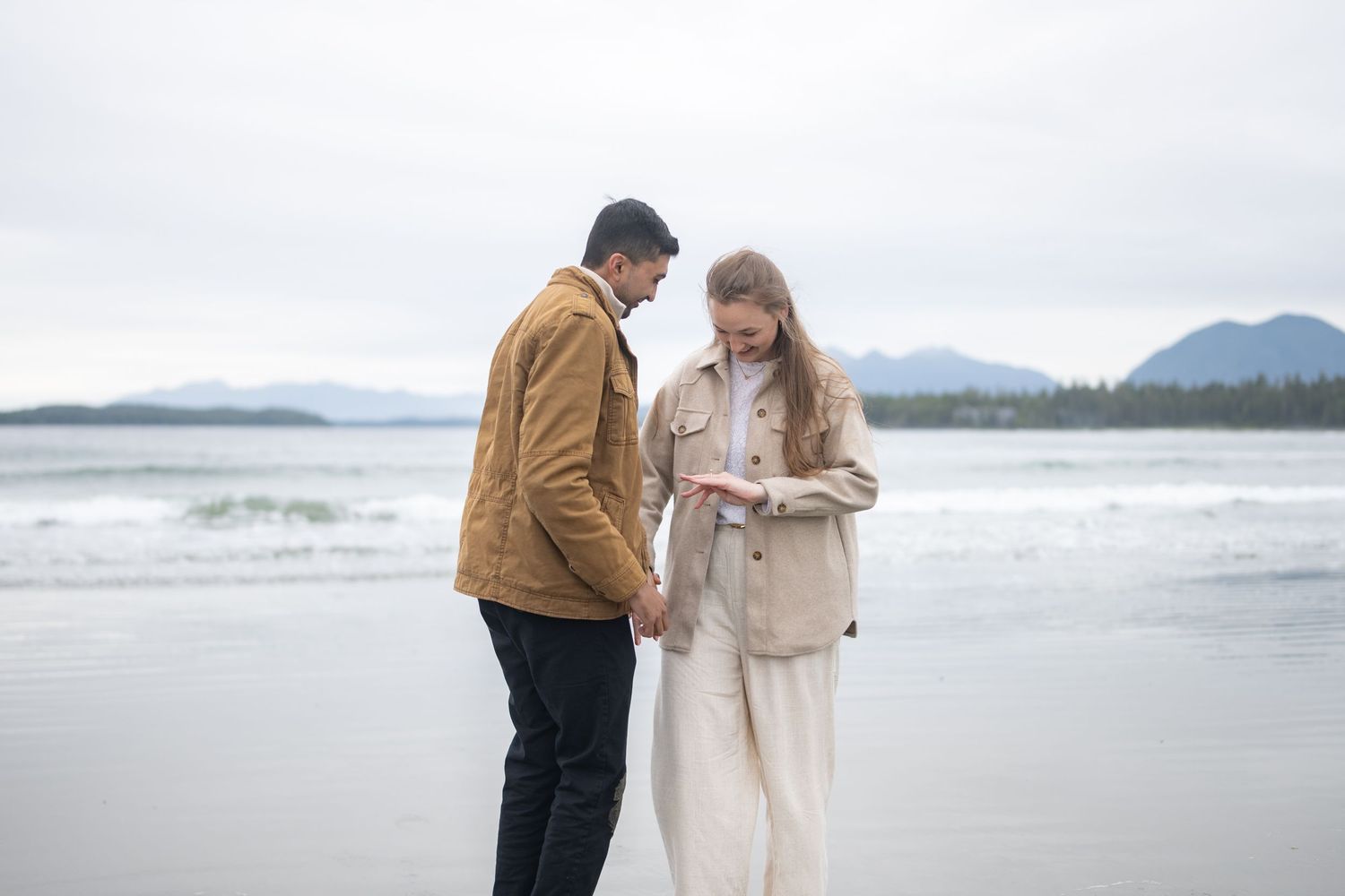 Couple sharing a romantic moment on a misty beach with mountains in the background.