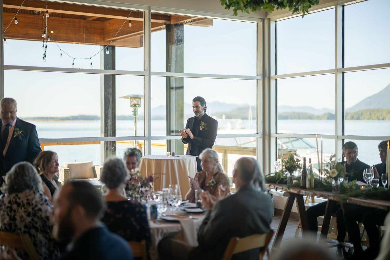 Wedding guests enjoy a reception dinner at an upscale waterfront restaurant with panoramic views.
