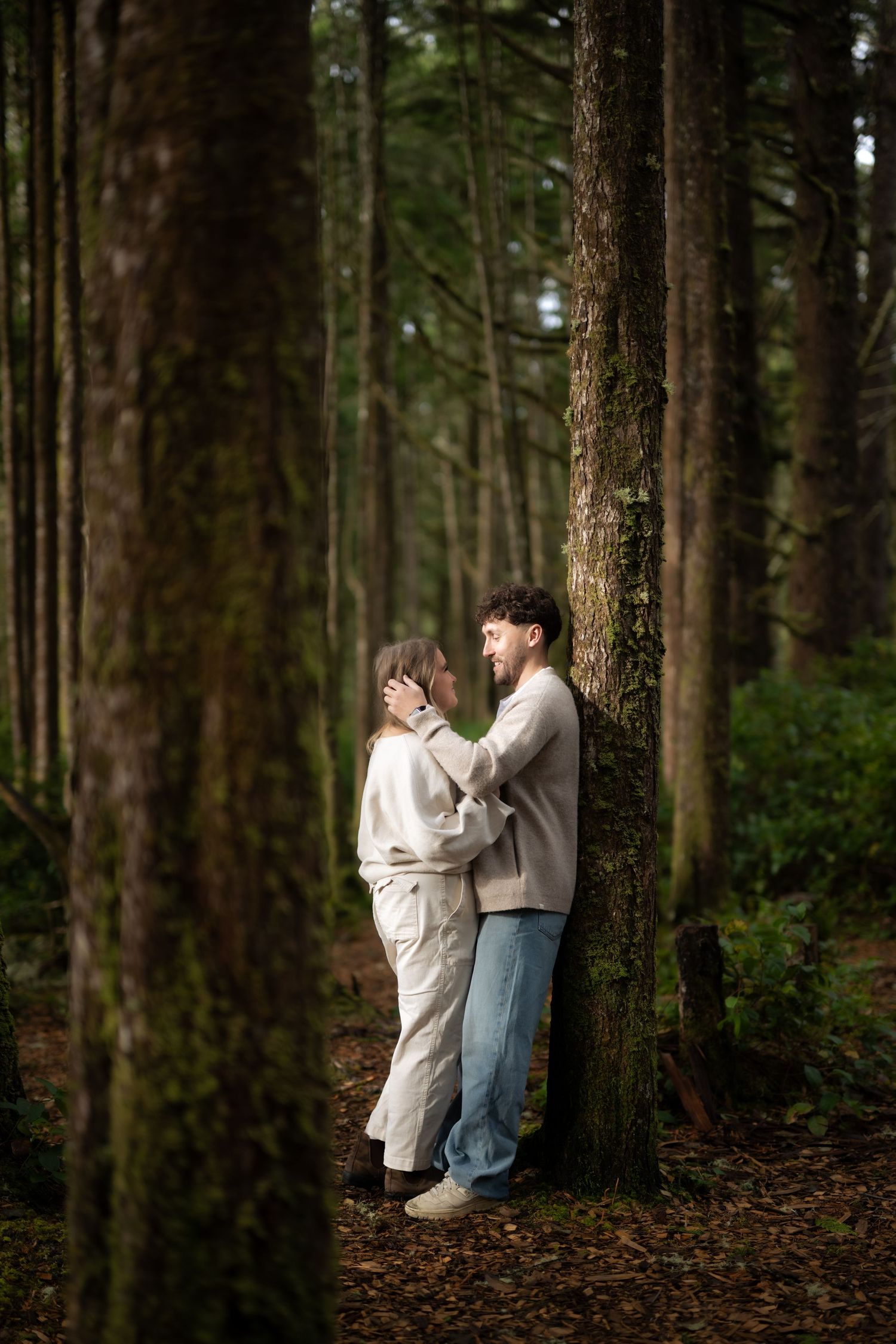 Couple in light colored clothing sharing intimate moment against forest backdrop.