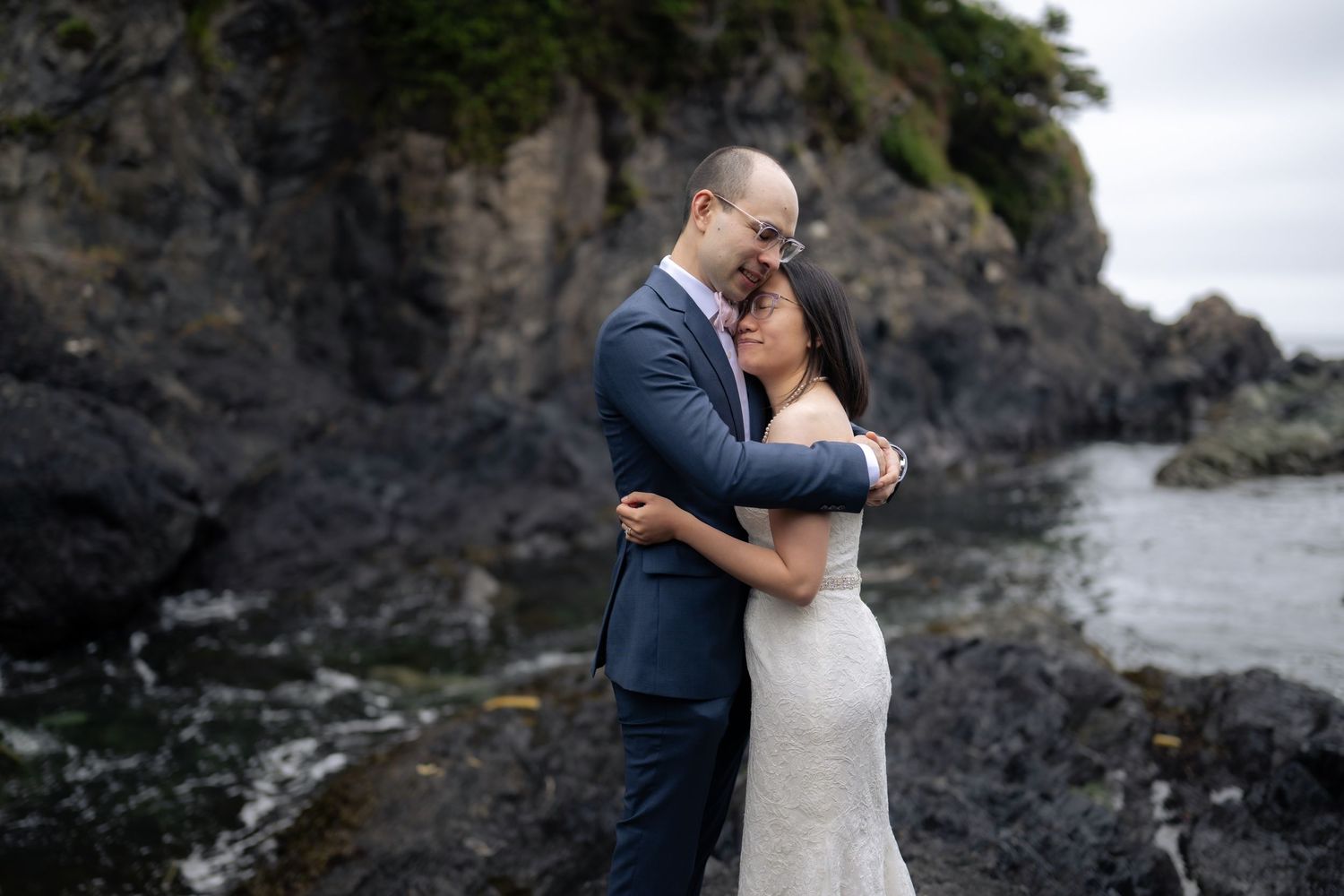 Intimate wedding moment captured against rugged coastal cliffs and crashing waves.