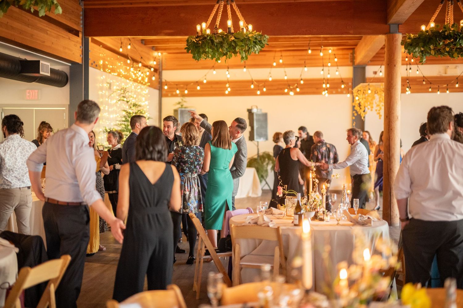 Wedding reception venue decorated with warm lighting and greenery in a rustic indoor space.