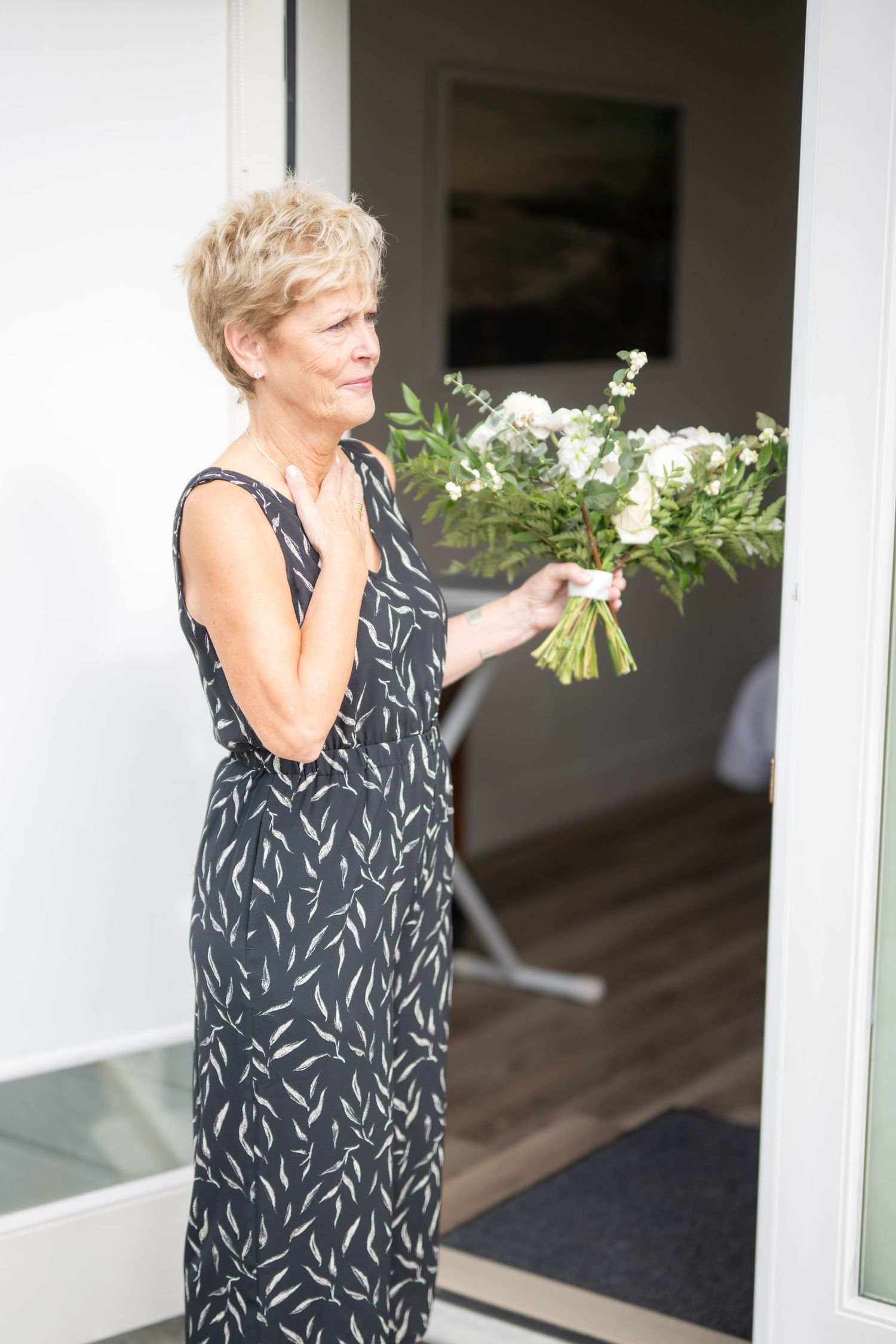 Wedding guest in patterned dress holding white floral arrangement near doorway.