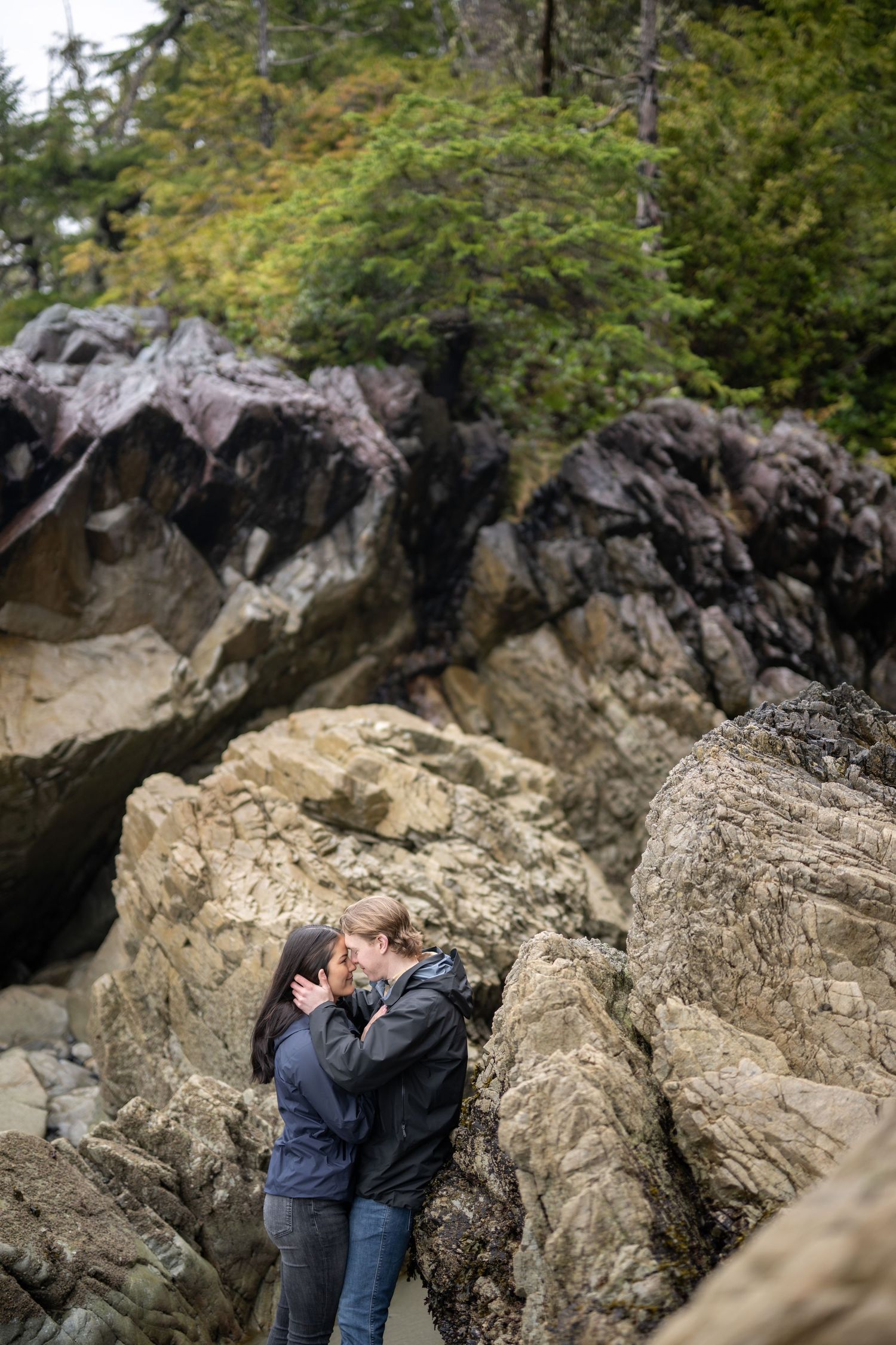 A tender embrace between two people among dramatic coastal rock formations.